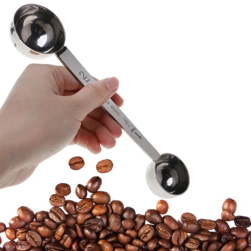 Hand holding a stainless steel measuring spoon over coffee beans on a white background